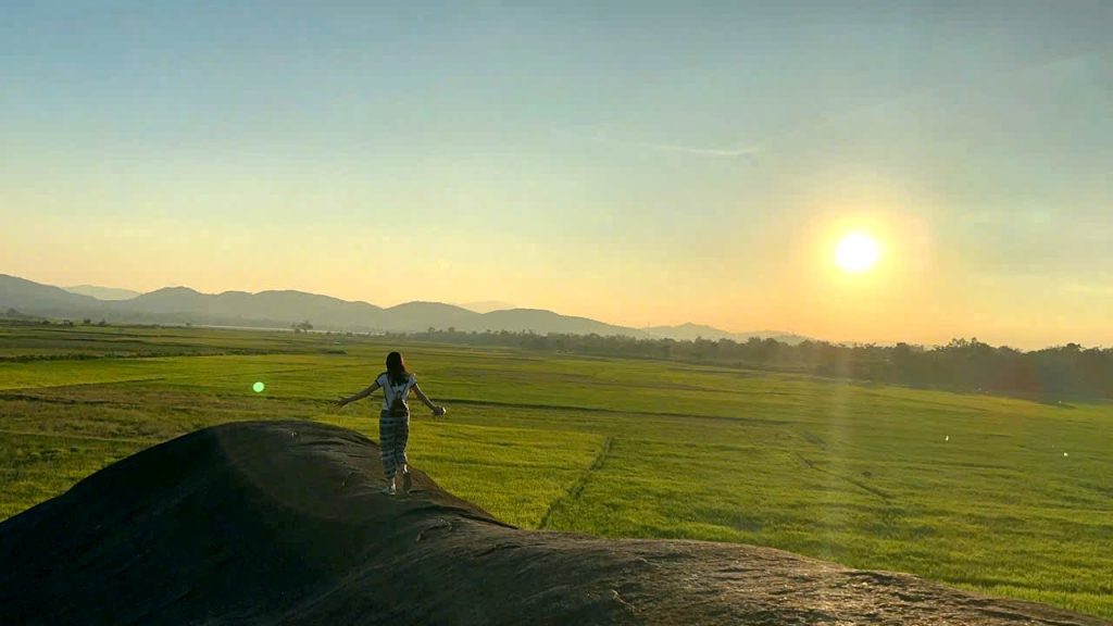 Traveler on a rock above the rice fields of Lak at sunset