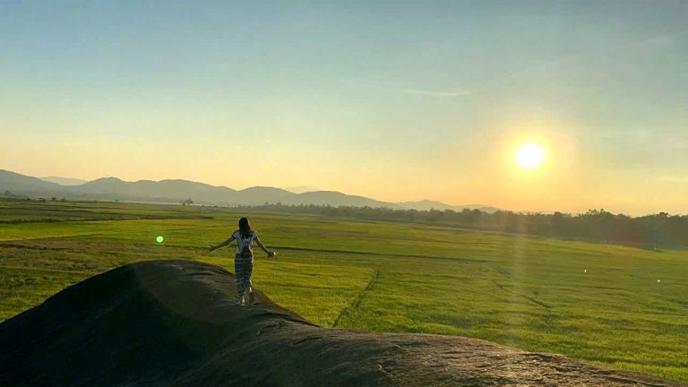 Traveler on a rock above the rice fields of Lak at sunset